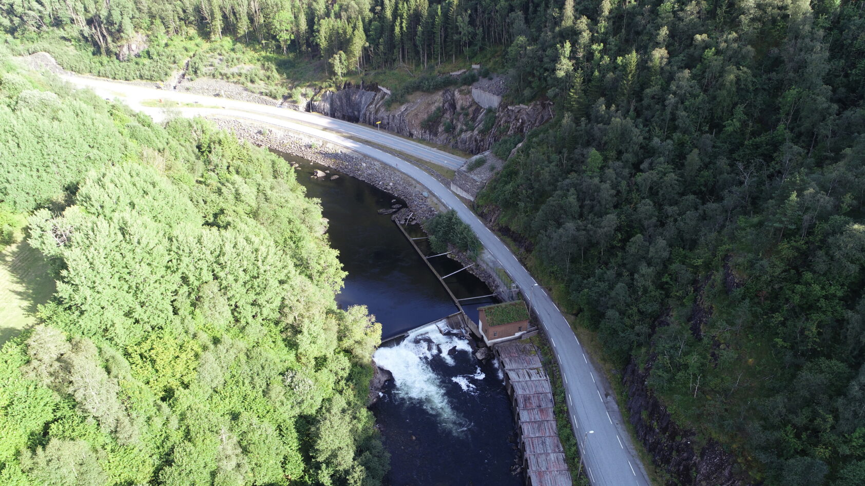 NORCE, Her ser vi kraftverket i Tysse. Inntaket til kraftverket er under bygningen til høyre., Kraftverket i Tysse inntak til kraftverket er under bygningen til høyre, <p>NORCE</p>, Dronebilde, elv med demning.