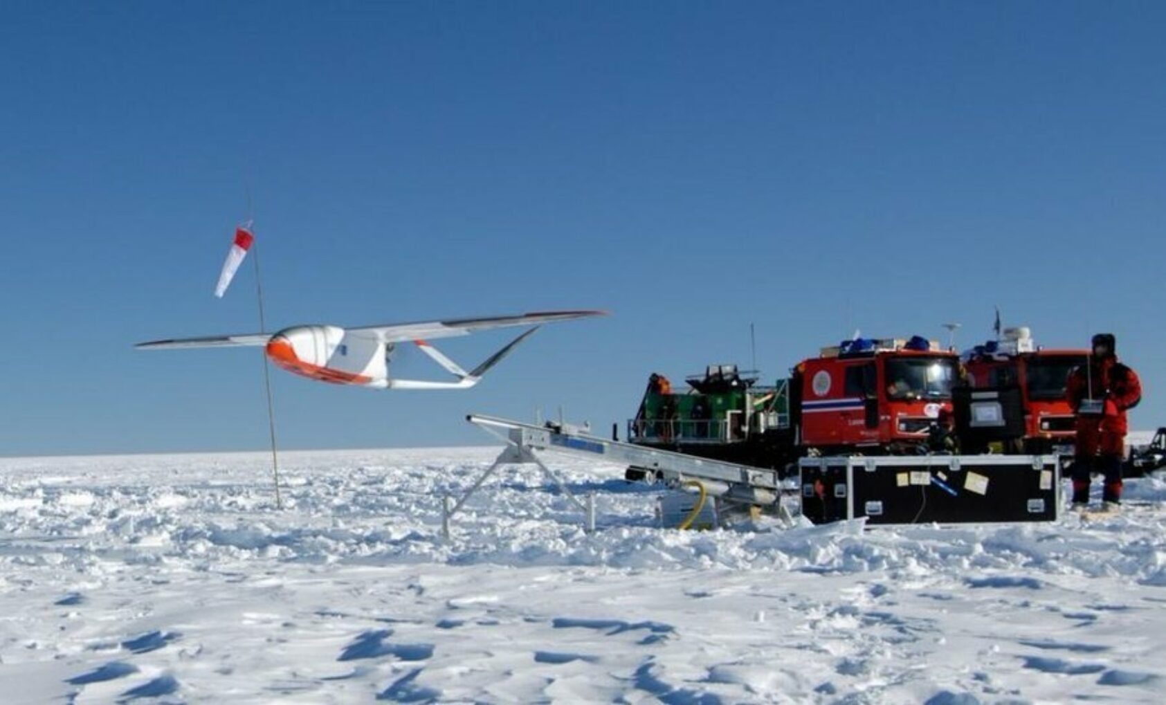 Jan-Gunnar Winther, I 2007 deltok NORCE på en norsk-amerikansk ekspedisjon fra Troll-stasjonen, gjennom det indre av Antarktis i retning Sydpolen., NORCE utviklet Roamer drone Foto Jan Gunnar Winther Norsk Polarinstitutt, <p>Jan-Gunnar Winther, Norsk Polarinstitutt</p>, I Antarktis - drone tar av fra utskytningsrampe for drone. Kjøretøy i bakgrunnen