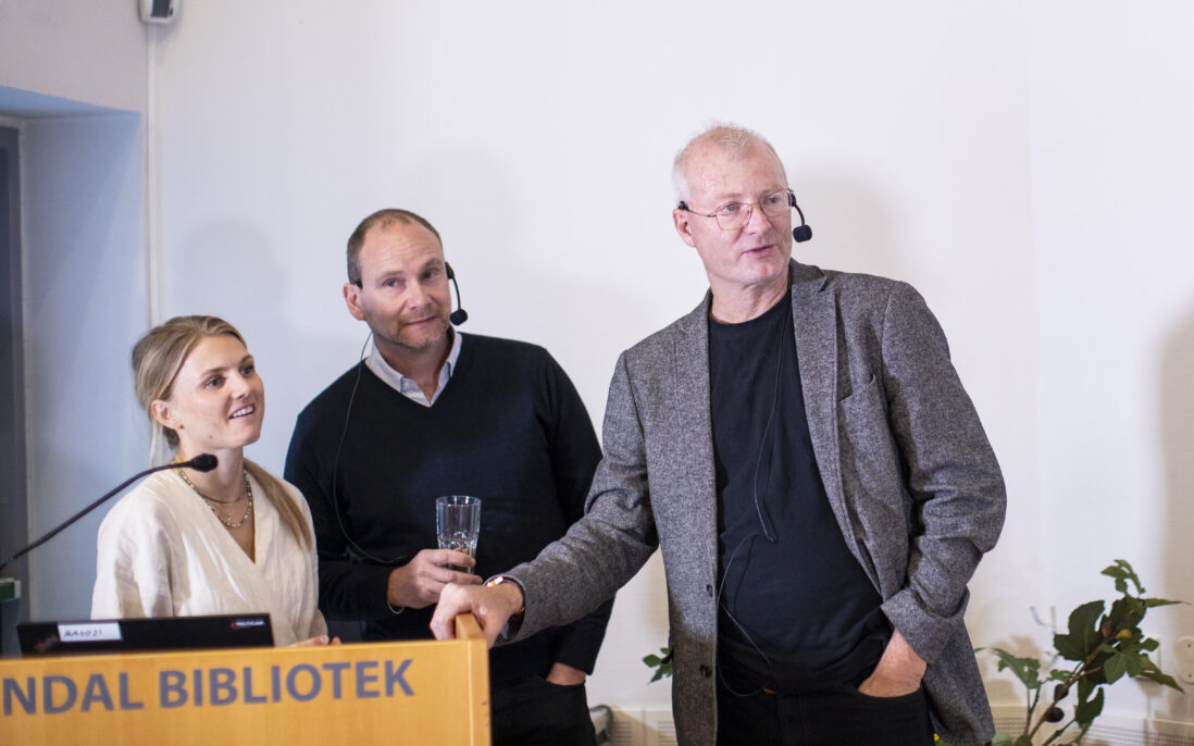 Tre smilende personer bak en talerstol