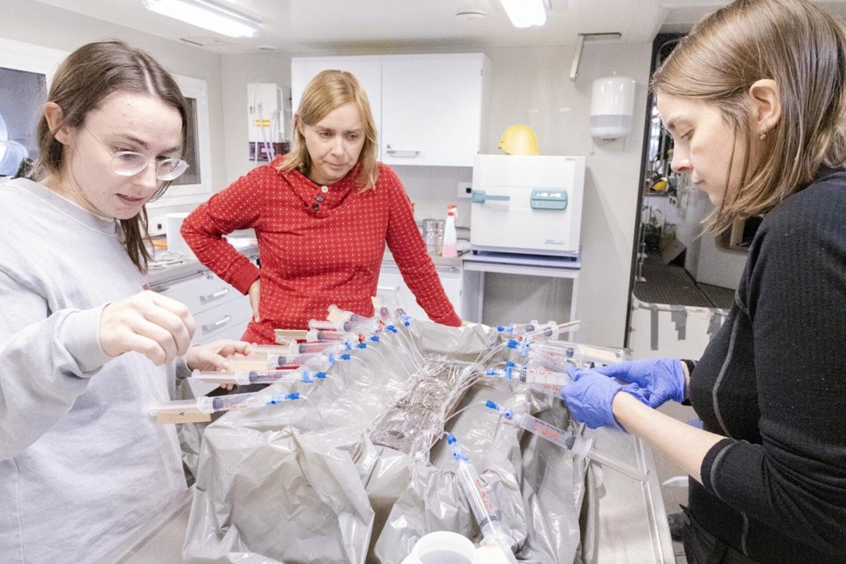 Daniel Albert, GoNorth/SINTEF, Hannah Rose Babel (UiB), Jasmin Schönenberger (NGU) and Amandine Tisserand (NORCE) at work sampling porewater from a sediment core. Porewater is water that is trapped in the sediements. It will be analysed to establish its chemical makeup, which will, together with DNA analyses help us understand which microorganisms inhabit the subseafloor., IMG 2095, ,