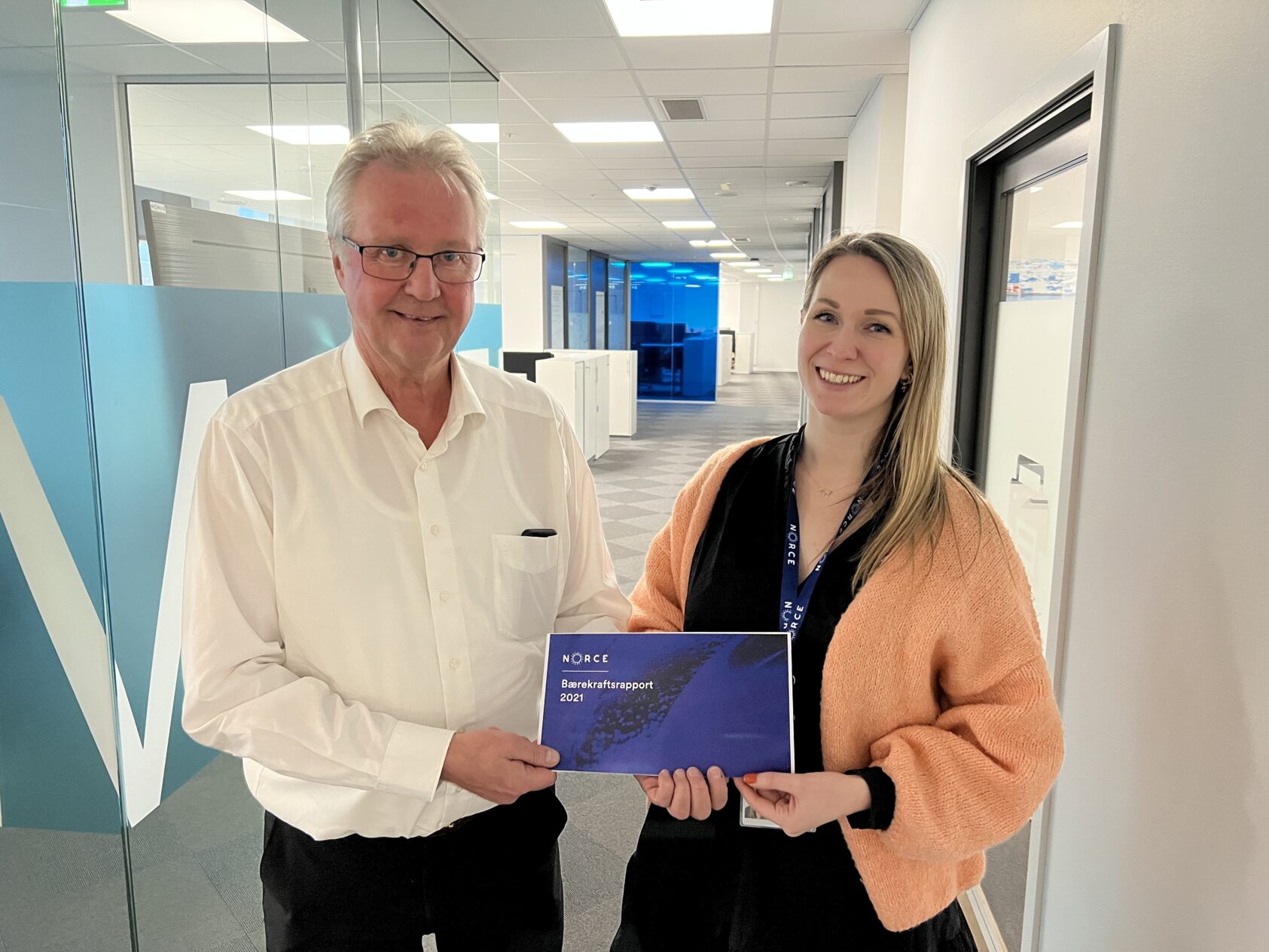 Camilla Aadland, kommunikasjonssjef NORCE, Bilde av NORCE sin konstituerte konserndirektør Thor Arne Håverstad og Lene K. Hansen, NORCE sin bærekraftsansvarlige ., Thor Arne og Lene, <p>Camilla Aadland, NORCE</p>, Mann i hvit skjorte holder en lilla papirrapport sammen med en dame i oransje jakke