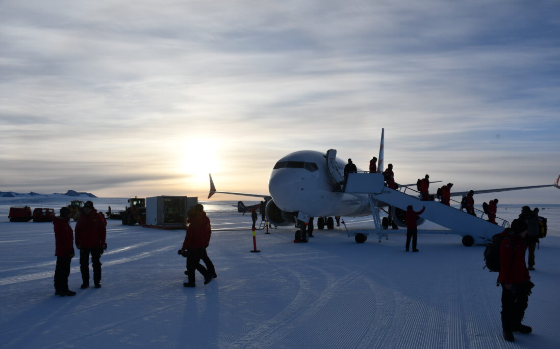 Mennesker går av fly mot sol og kveldshimmel.